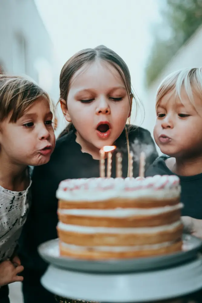 Tres niños pequeños soplan juntos las velas de una tarta de cumpleaños.